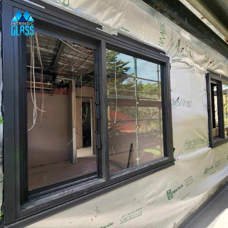 Residential window glass replacement in progress with black aluminium frames and exposed wall wrap.