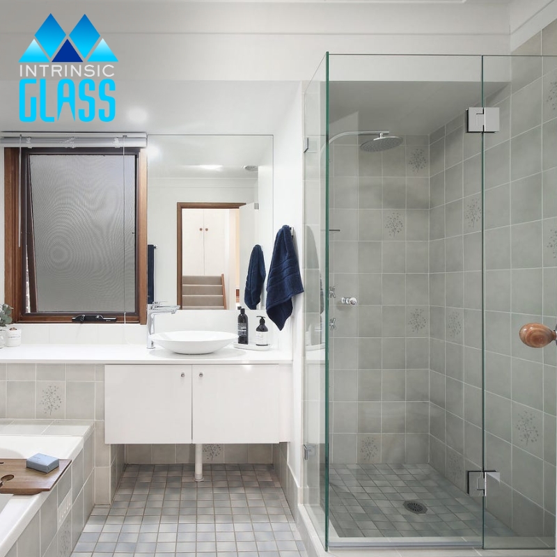 A modern bathroom interior featuring a frameless shower screen in Dudley made of clear glass. The shower screen allows for an unobstructed view of the tiled shower interior and complements the white sink.