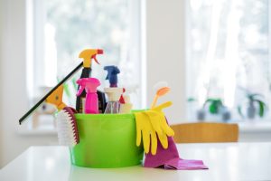 A green bucket filled with various cleaning supplies, including spray bottles, a squeegee, scrub brushes, rubber gloves, and cleaning cloths. These tools are essential for achieving clean glass shower screens, ensuring a spotless and streak-free finish.