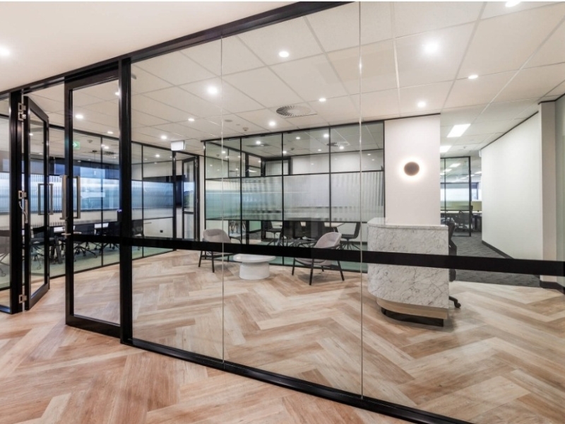 Glass-walled offices with black frames optimising office space, enhancing design, and separating meeting areas in a contemporary setting.