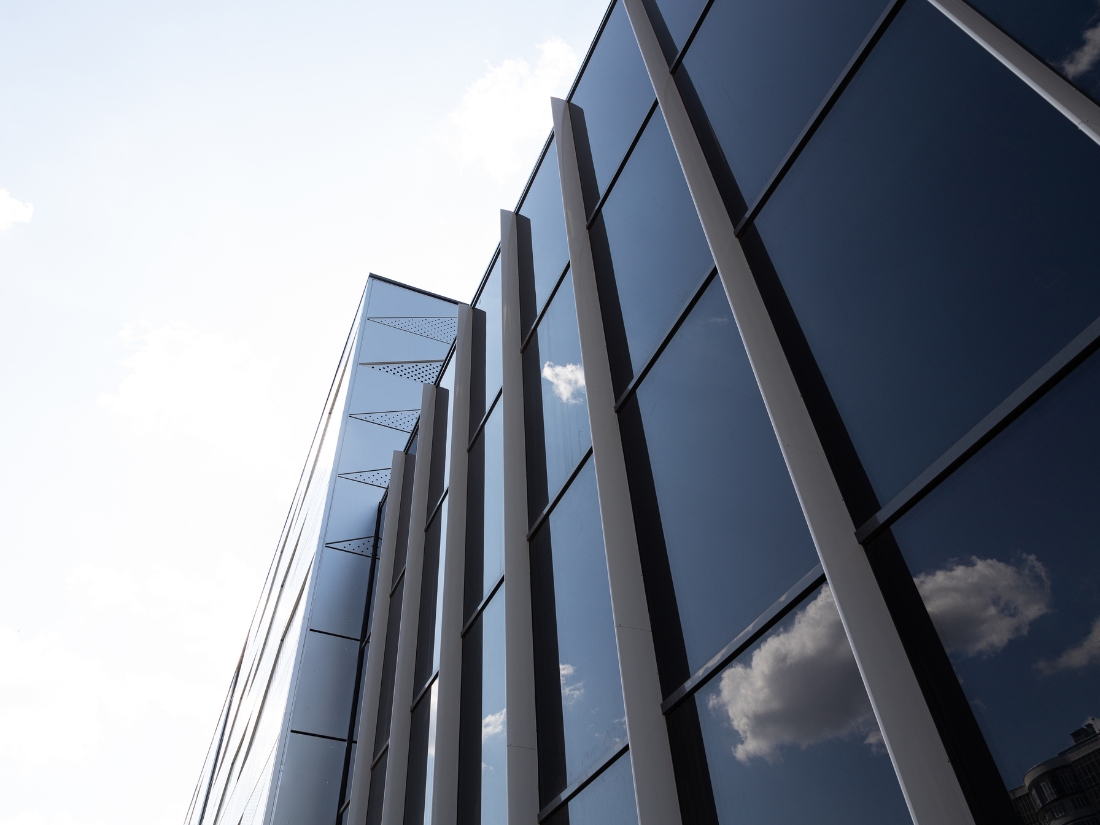 A modern building with a sleek black glass wall reflecting the sky.