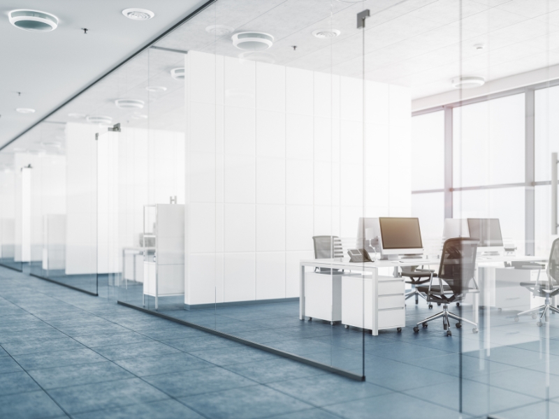 Bright open-plan office with floor-to-ceiling glass walls in office, minimalist furniture, and natural light enhancing the modern workspace design.