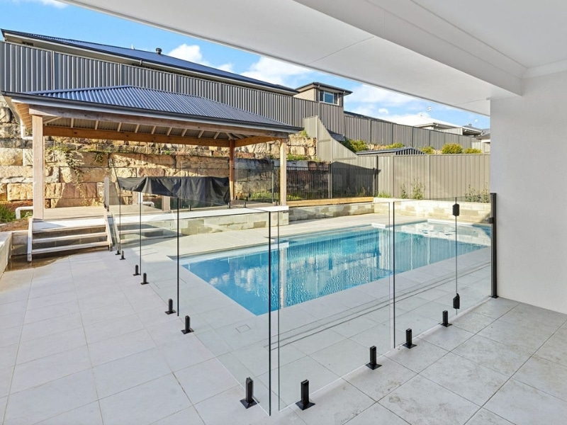 Modern backyard with coloured glass pool fencing enclosing a rectangular swimming pool and a covered seating area in Sydney.