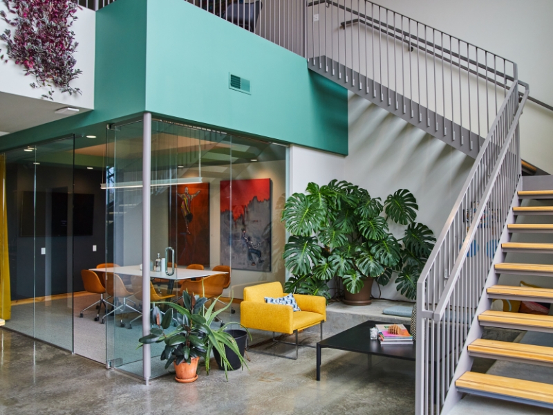 Colourful and stylish glass meeting room in a creative office space with plants, artwork, and modern furnishings.