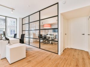Compact office featuring black-framed half glass partition enclosing a meeting room with clear views and warm lighting.