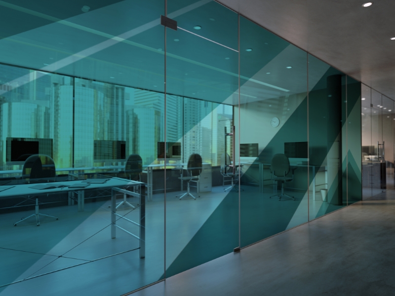 Contemporary office with tinted frameless glass partition, sleek desks, and city skyscraper reflections.