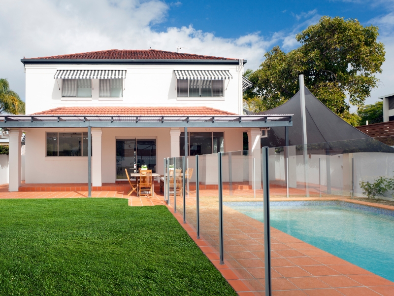 Residential home with tiled patio and curved glass pool fencing enclosing a private swimming area.