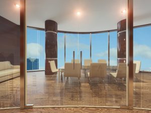 Luxury boardroom with frameless glass partition, wooden flooring, cream chairs, and panoramic city skyline views.