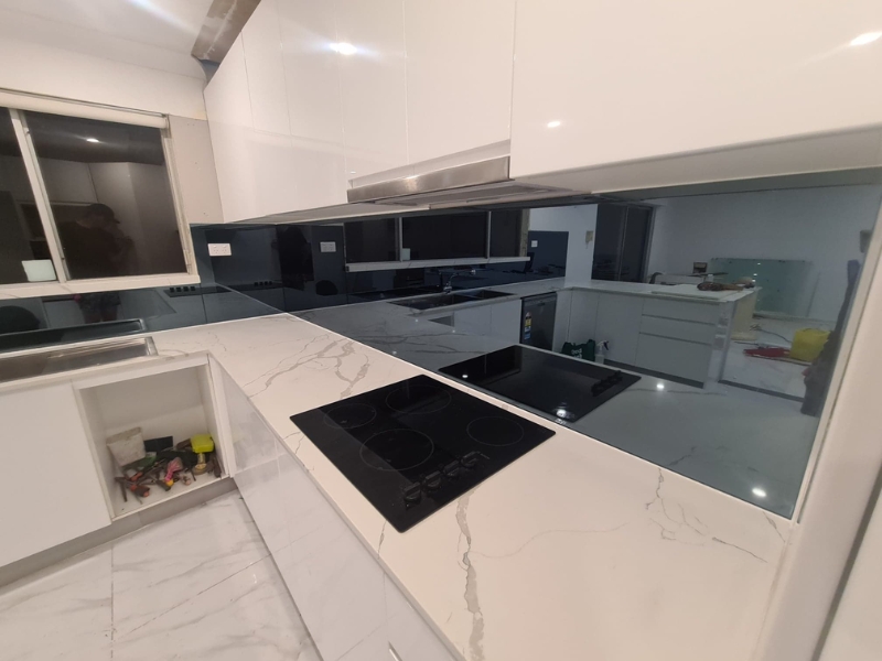 Reflective black glass wall created by installing a glass splashback above cooktop