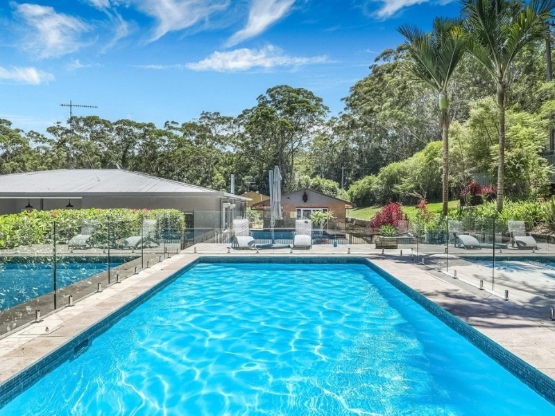 Outdoor swimming pool area with surrounding glass pool fence panels and landscaped garden.